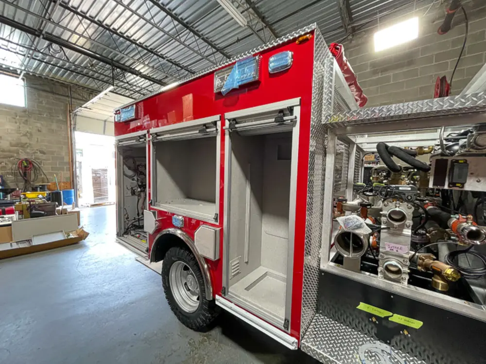 Exterior view of small fire truck showing cab, body compartments, and wheel/tire area.